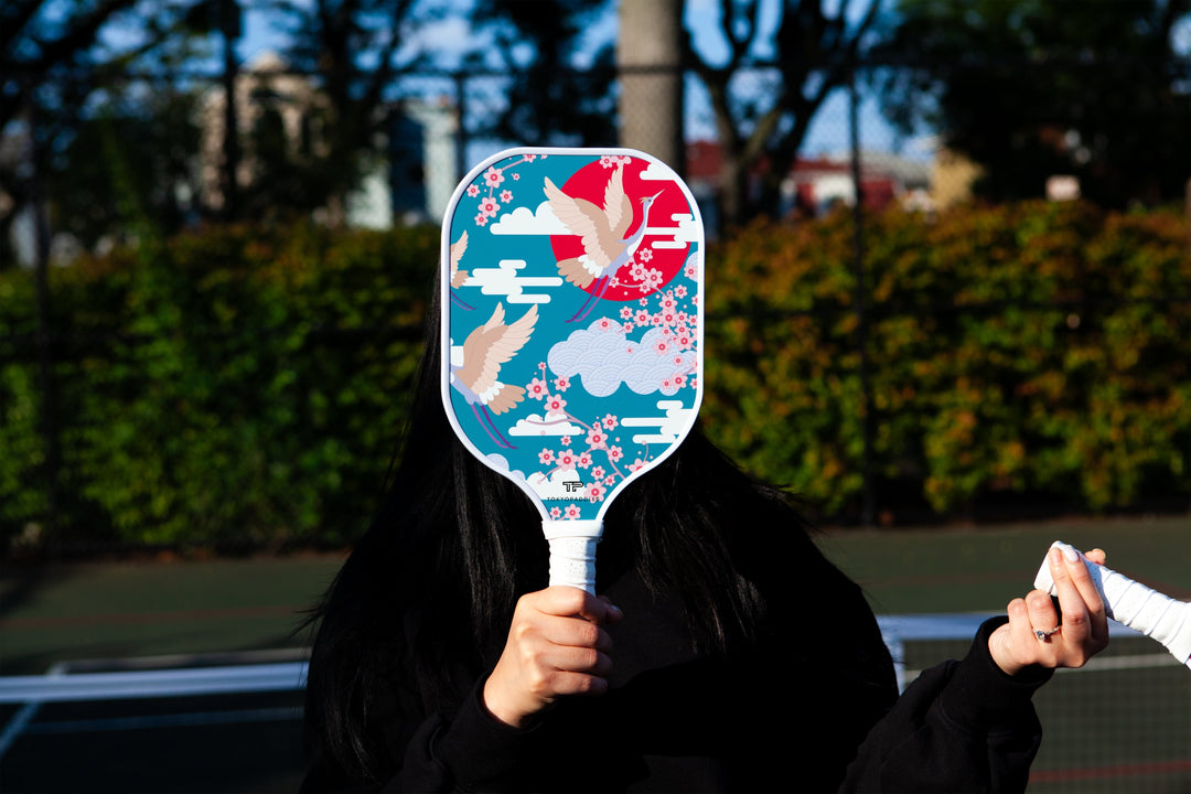 Girl covering her face with a crane daze japanese inspired pickleball paddle.